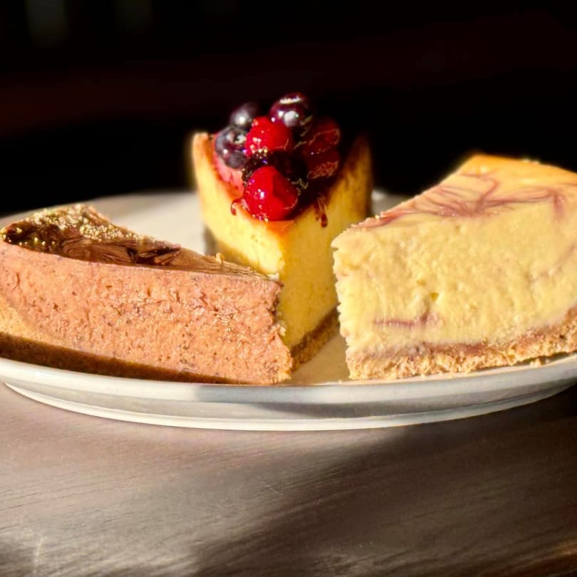 Three slices of cheesecake, including berry, chocolate, and swirled, on a white plate.