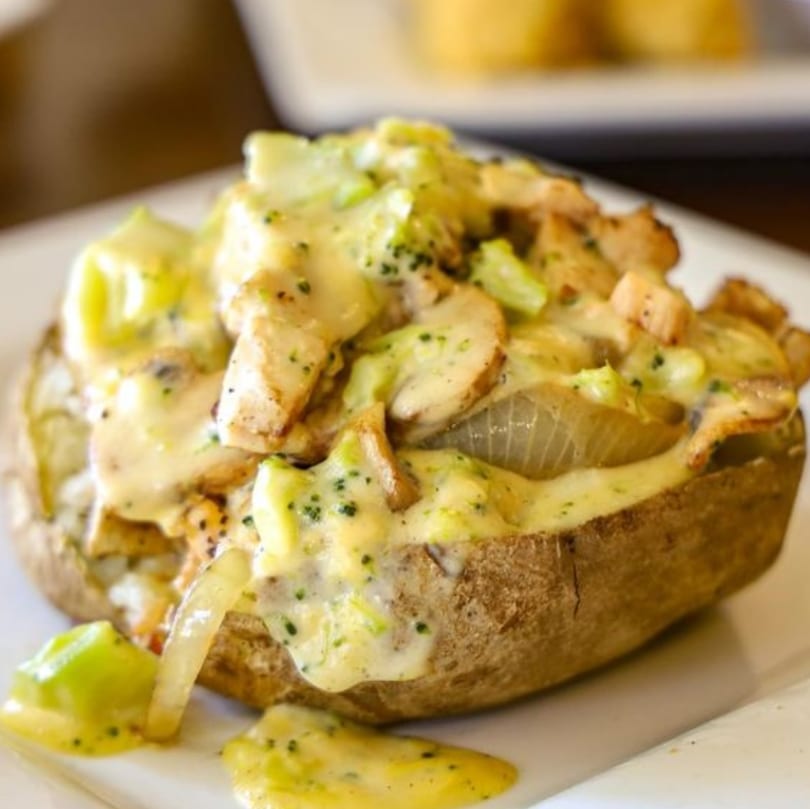A baked potato topped with chicken, broccoli, onions, and a creamy cheese sauce.