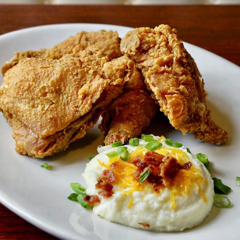 Crispy fried chicken pieces with a side of mashed potatoes topped with cheese, bacon, and chives.