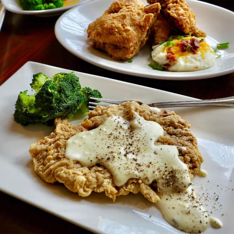 Chicken fried steak with gravy and broccoli, with fried chicken and mashed potatoes in the background.